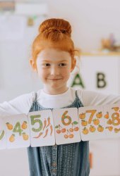 Young girl showcasing number cards in a vibrant classroom setting.