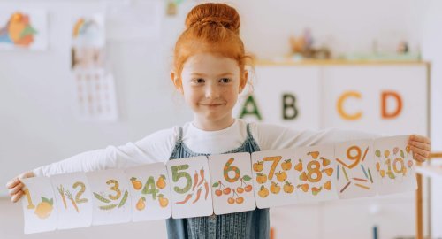 Young girl showcasing number cards in a vibrant classroom setting.